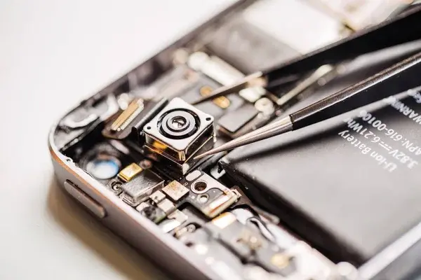 Técnico reparando la cámara de un celular con herramientas de precisión