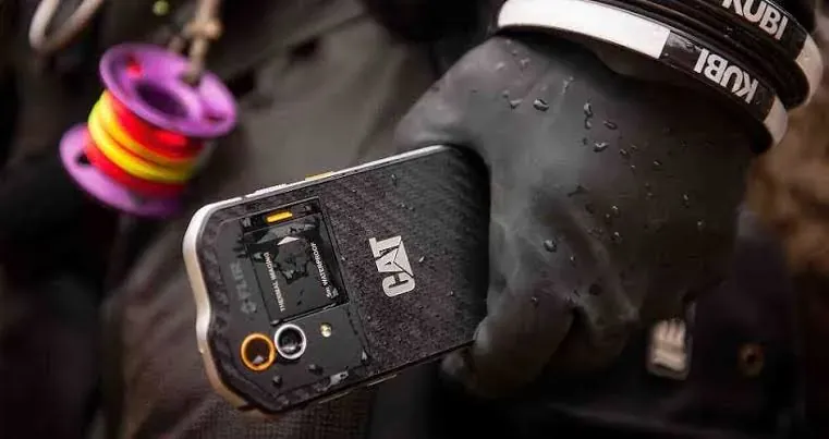 Celular resistente CAT sostenido por una mano con guante de trabajo
